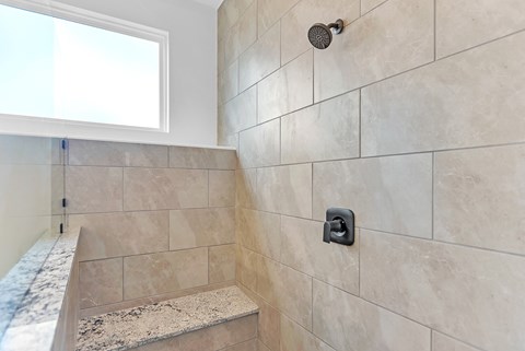 A shower area with a marble tile wall and a marble bench seat.