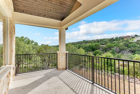 A balcony with a black railing and a view of a green landscape.