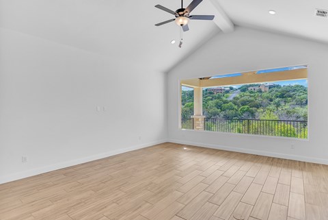 A room with a ceiling fan and a window overlooking a green landscape.