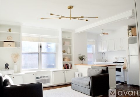 A living room with a black couch and a white kitchen in the background.