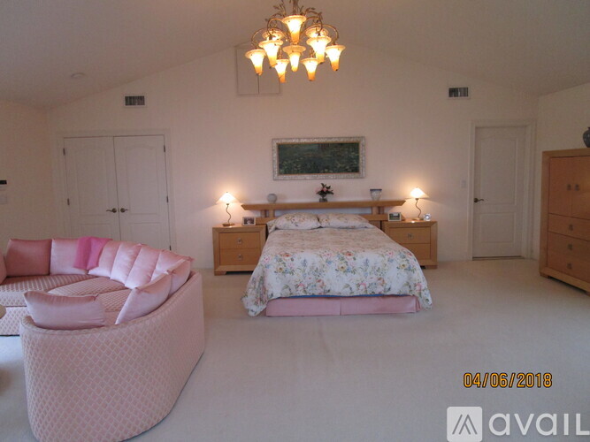 A bedroom with a large bed and a pink chair.