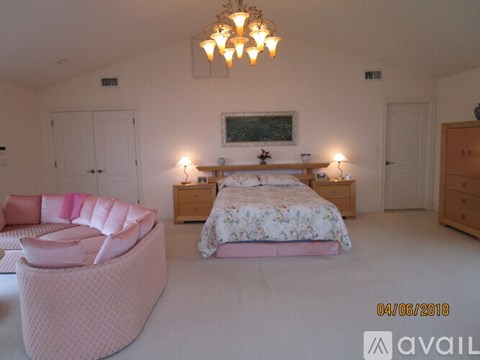 A bedroom with a large bed and a pink chair.