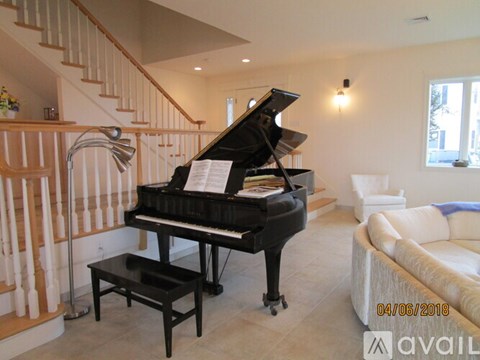 A grand piano is in a living room with a white couch and a staircase.