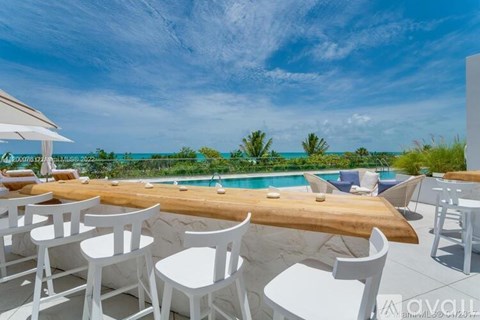 A white table and chairs are set up on a patio overlooking a pool and the ocean.