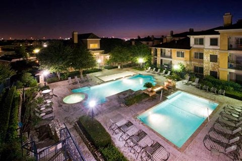 A swimming pool surrounded by chairs and trees at night.