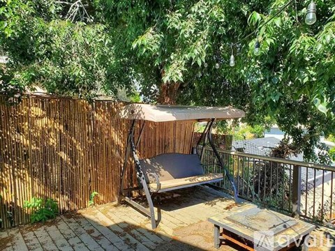 A wooden swing set is situated on a patio under a tree.