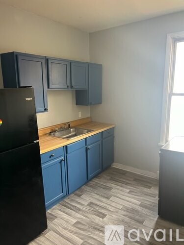 A kitchen with blue cabinets and a black refrigerator.