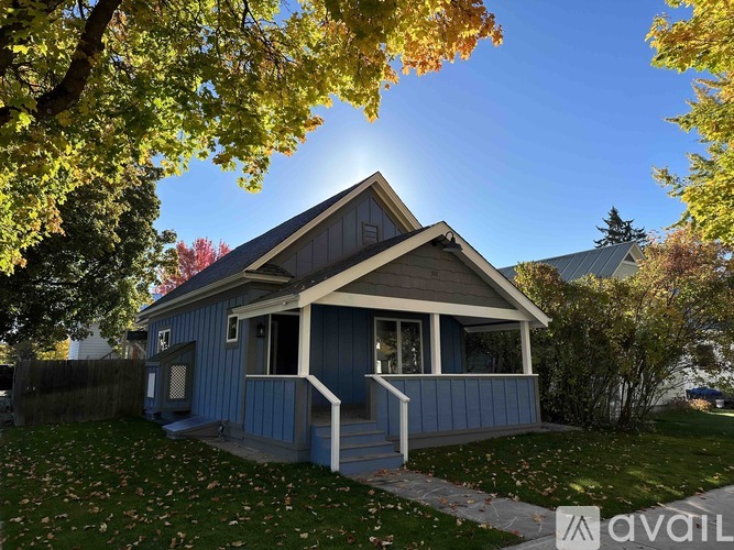 A small blue house with a porch and a tree in front.
