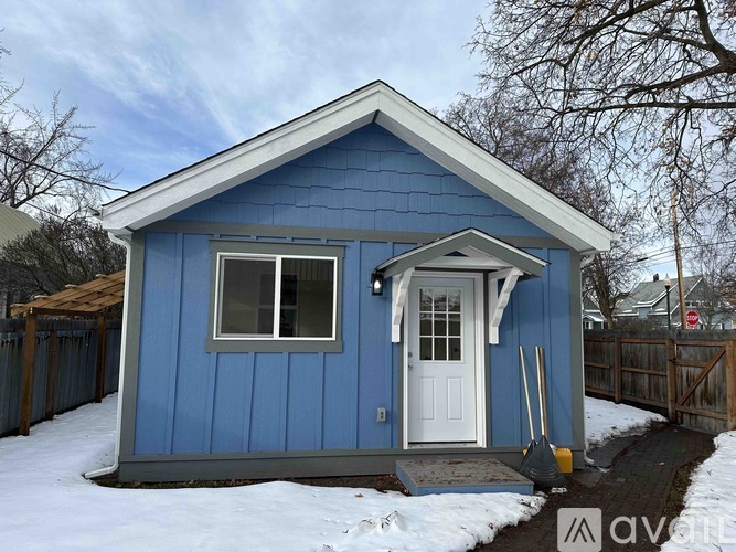 A small blue house with a white door and a shovel in front.