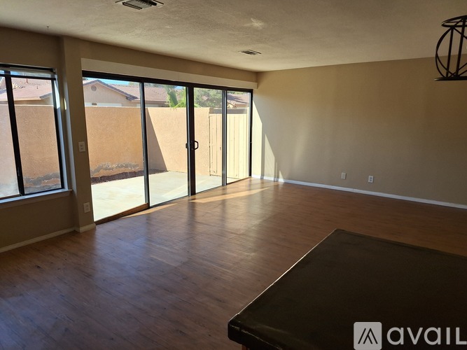 A room with a brown floor and a large window with a view of a fence and a house.