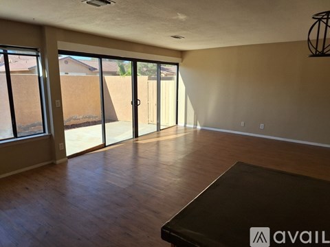 A room with a brown floor and a large window with a view of a fence and a house.