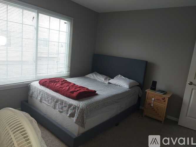 A bedroom with a bed, a nightstand, and a window with blinds.