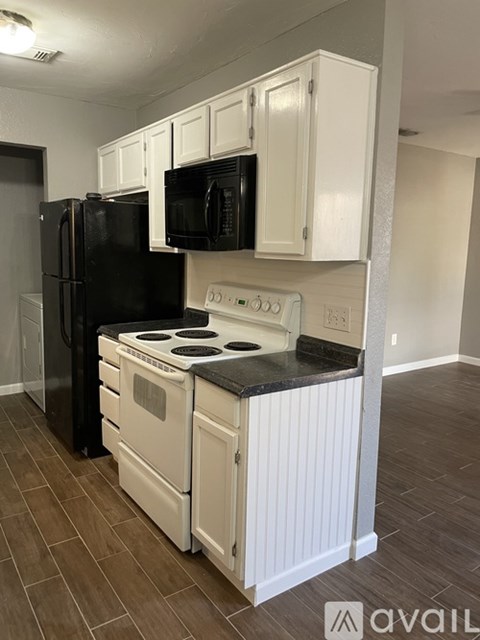 A black refrigerator and microwave in a kitchen with white cabinets.