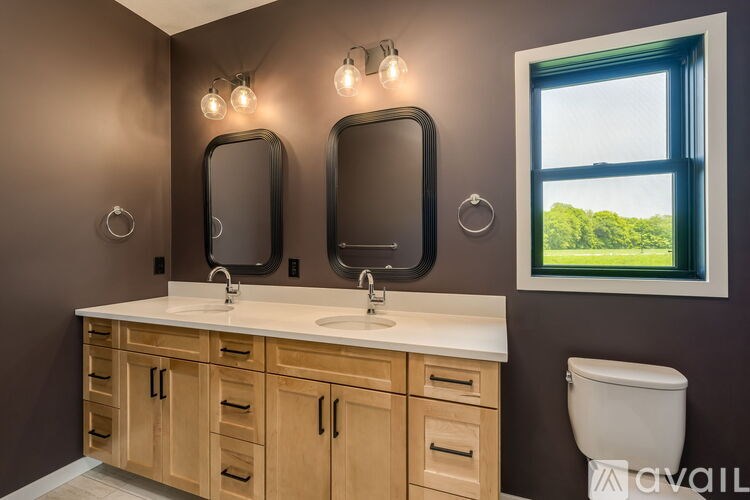 A bathroom with brown walls, a white counter top, and a window with a view of trees outside.