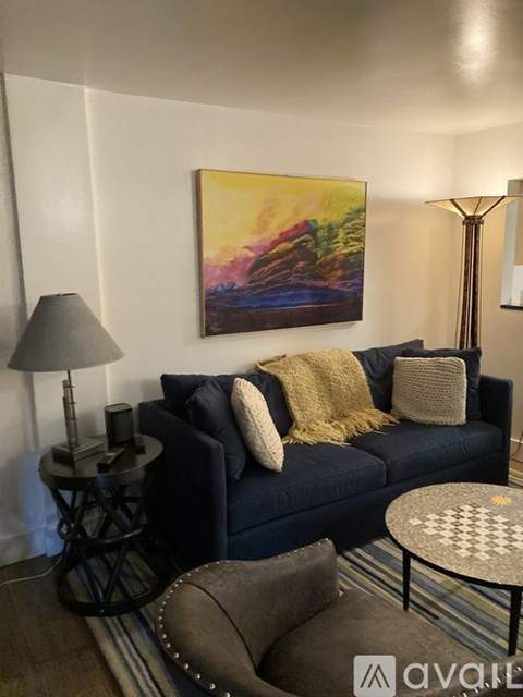 A living room with a blue couch, a lamp, and a painting on the wall.
