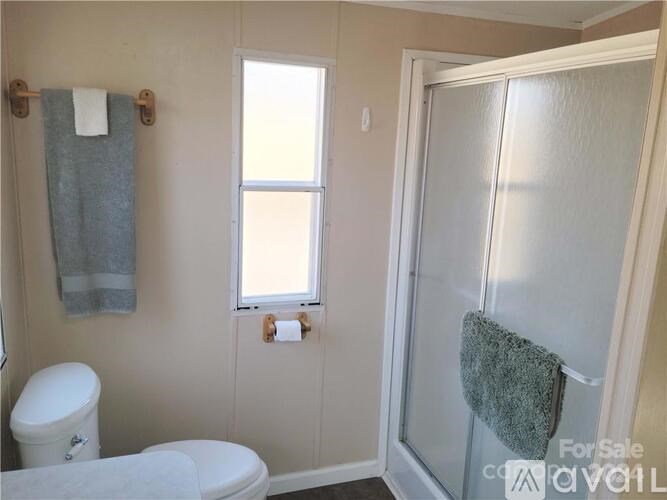 A bathroom with a toilet, a window, and a towel hanging on the door.