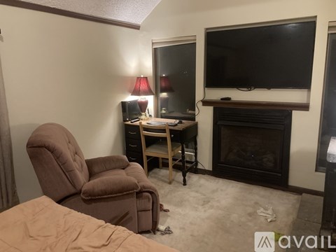 A living room with a brown recliner, a small table with a lamp, and a flat screen TV mounted above a fireplace.