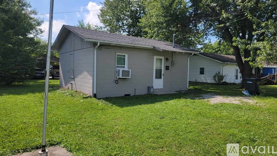 A small house with a grey roof and a white door is surrounded by green grass.