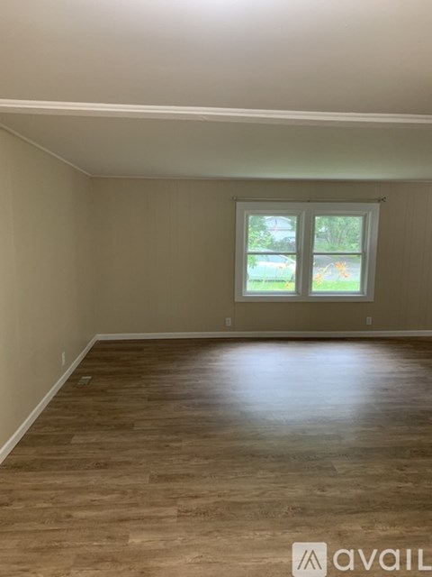 A room with wooden flooring and a window showing a view of trees and a lawn.