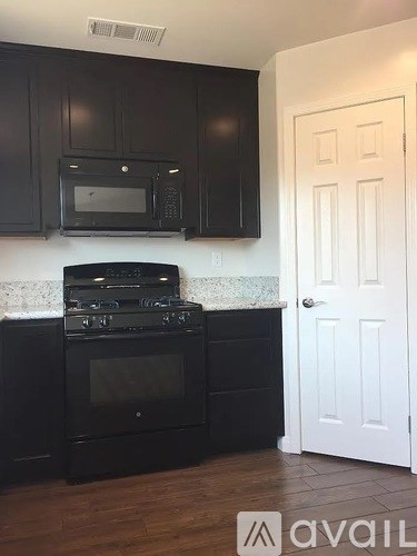 A kitchen with black cabinets and appliances, a white door, and a white subway tile backsplash.