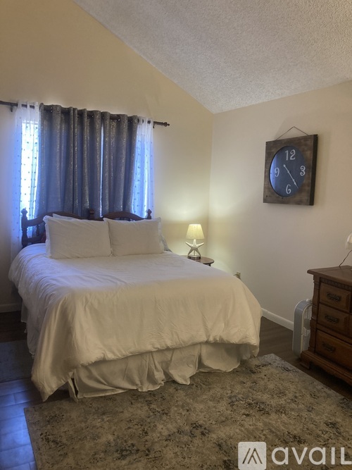 A bedroom with a bed, nightstand, and clock on the wall.