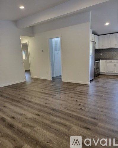 A spacious room with wooden flooring and a kitchen area in the background.