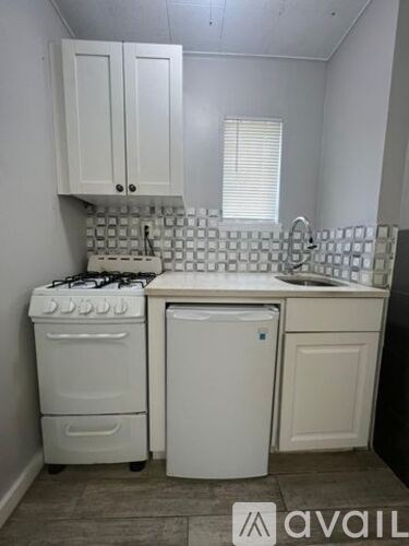 A small white kitchen with a stove, sink, and cabinets.