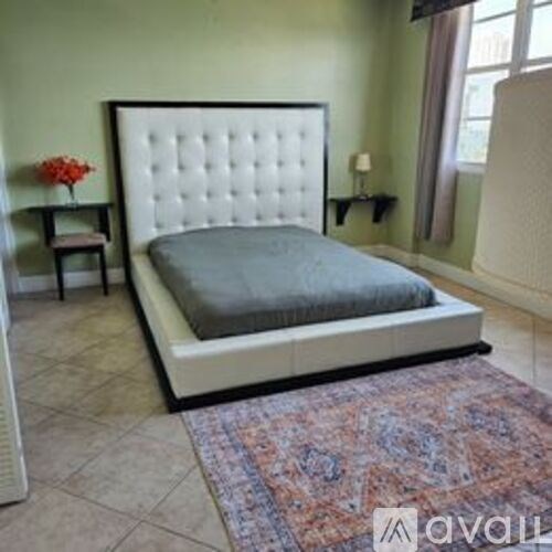 A bed with a white headboard and grey bedspread is in a room with a patterned rug.