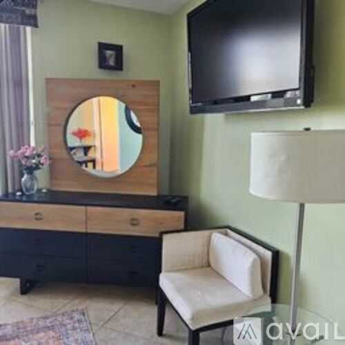 A black TV is mounted on a green wall above a white chair.