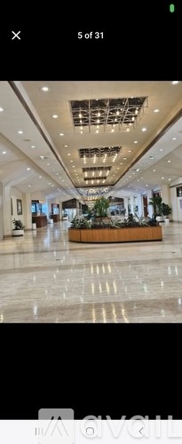 A long, rectangular wooden table with a green plant on top is in the center of a spacious room with a marble floor.