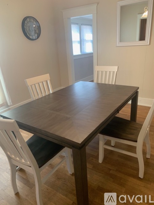 A dining table with four chairs and a clock on the wall.