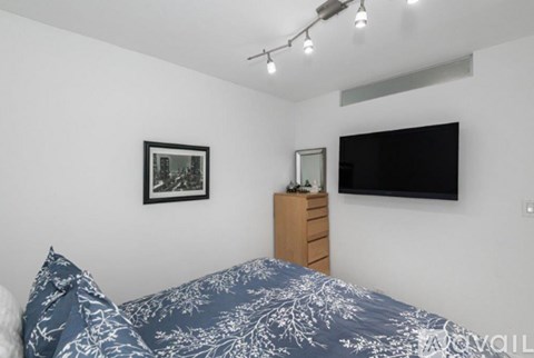 A bedroom with a bed, a dresser, a picture on the wall, and a flat screen TV mounted above the dresser.