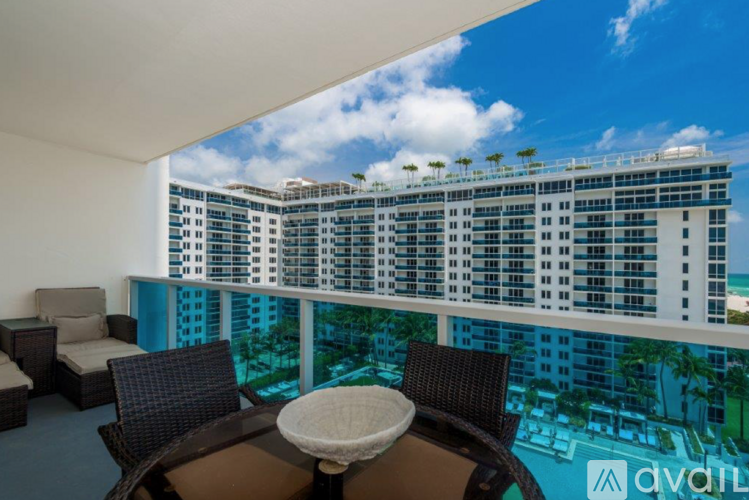 A balcony with a table and chairs overlooking a pool and a large building.