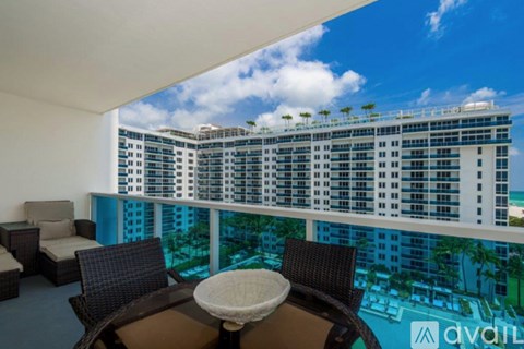A balcony with a table and chairs overlooking a pool and a large building.