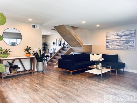 A living room with a black couch and a wooden staircase.