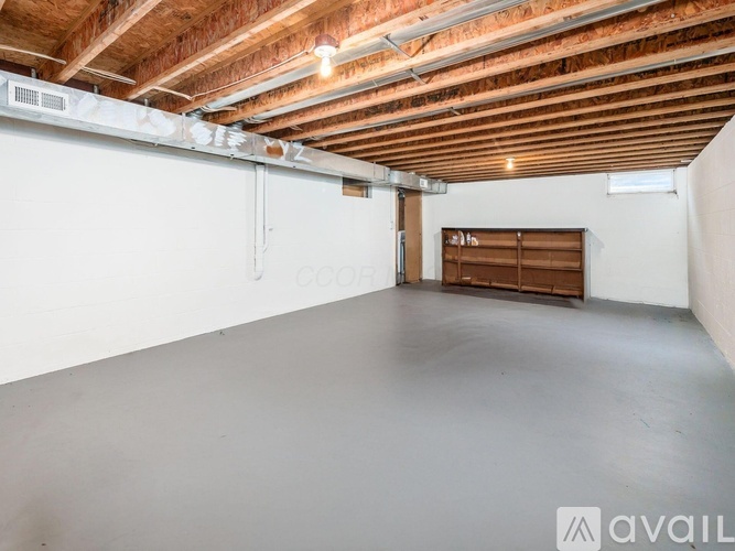 A spacious room with wooden ceiling and white walls, featuring a window with wooden blinds and a white door.