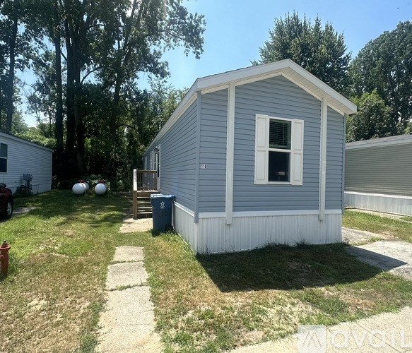 A small grey house with a white window and a door is surrounded by a grassy area.