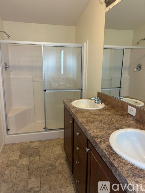 A bathroom with a tiled floor, a double sink vanity, and a walk-in shower.