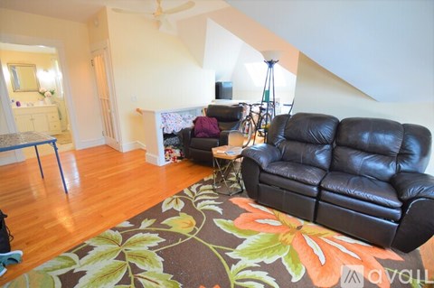 A living room with a black leather couch and a rug with leaves on it.