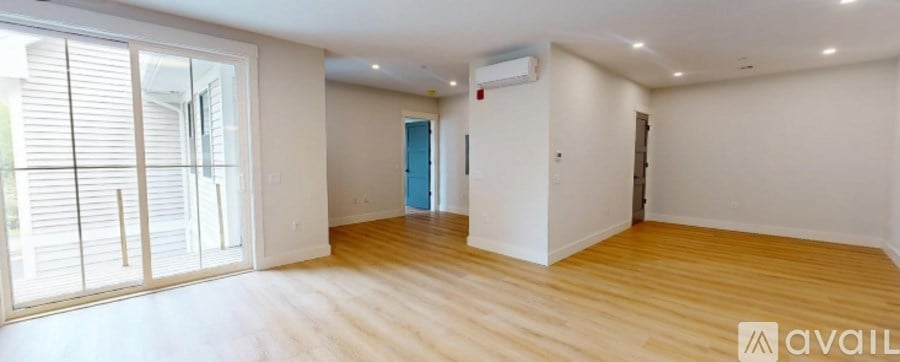 A spacious room with wooden floors and a large window with blinds.
