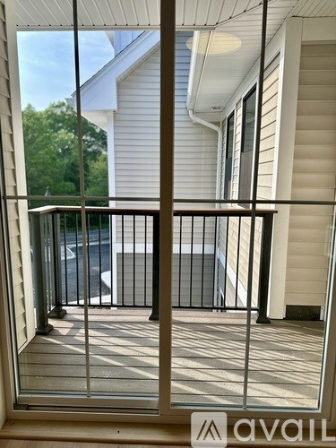 A balcony with a metal railing and a view of a white house and a car.