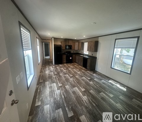 A room with a wooden floor and a kitchen area in the background.