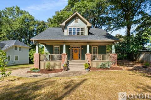 A house with a front porch and a brown door is surrounded by greenery.