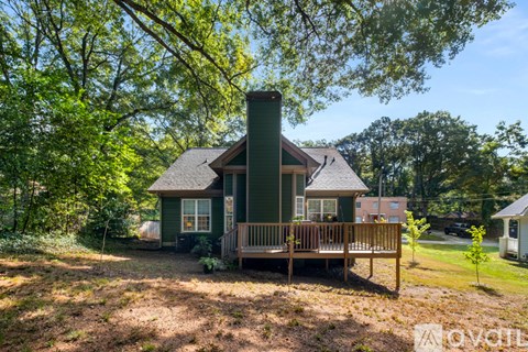 A green house with a porch and a chimney is surrounded by trees.