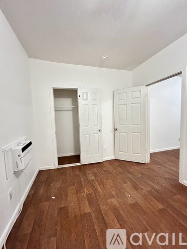 A room with wooden floors and white walls, with a door on the left and a closet on the right.