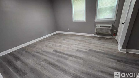 A room with grey walls and a grey floor with a window and air conditioner.