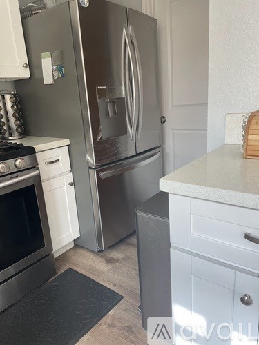 A stainless steel refrigerator stands in a kitchen with white cabinets.