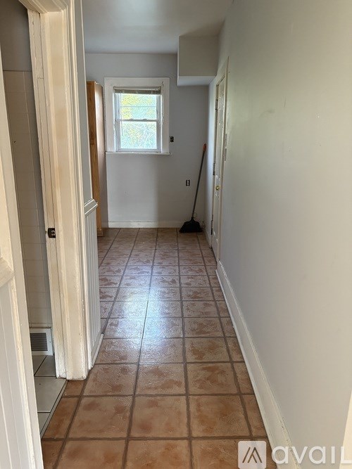 A hallway with tiled flooring and a broom in the corner.