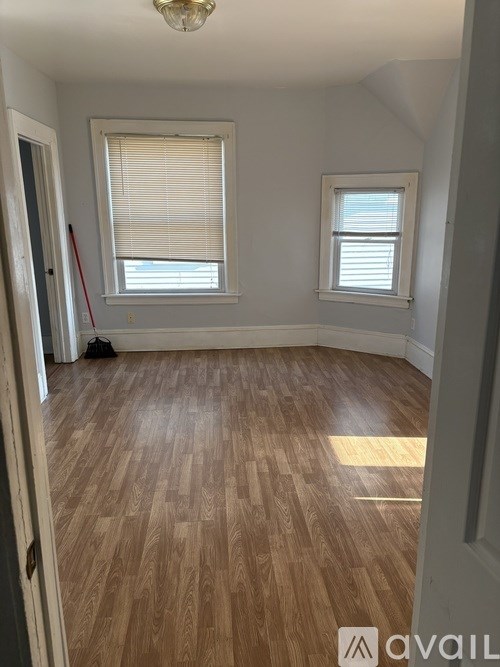 A room with wooden flooring and two windows.
