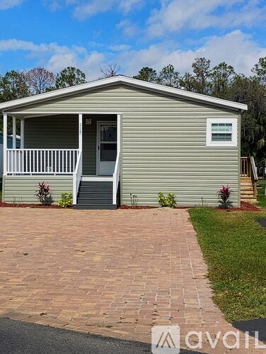 A small house with a grey siding and a white porch.